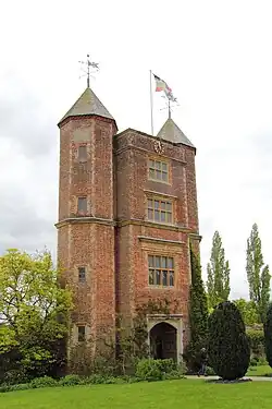 a high tower of red brick with two pyramid roofs and a flag flying