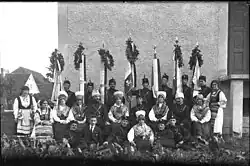 Uniformed men and women wearing folk costumes posing for a photo with flags in the background