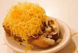 small oval white plate with cheese coney showing bun, hot dog, sauce, and shredded cheese