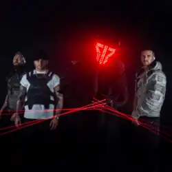 A photograph of the band standing looking at the camera, with member Apocalypse DJ wearing a red LED mask and lasers coming from devices on his hands