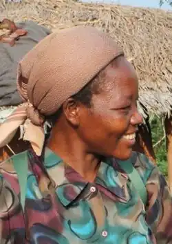Angélique Namaika smiling in a village, wearing a green shirt and brown headdress.