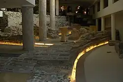 Columns and Roman brick and stone ruins on the ground floor of a hotel lit by yellow lighting.