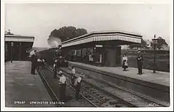 Side platform to left and island platform to right with canopies. Workers on the track and passengers on the platform with a steam train approaching.