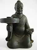A candle stick holder depicting a man in a robe with a youren opening, Southern dynasty (420-589 AD).