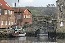 Two stone bridges, one behind the other, with a small beck passing underneath and emptying into a larger body of water