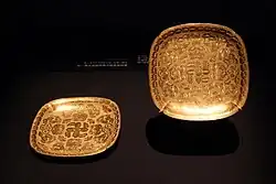 A pair of square lobed gold dishes with chased insects, flowers, and knotted ribbons