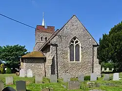 A medieval church surrounded by a cemetery. There are trees in the right foreground and left background, and a blue sky