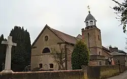 A small brick church surrounded by trees, with a war memorial in the foreground