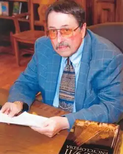 Atkins at a table with paper in his hands, with his book The 9/11 Encyclopedia in front of him