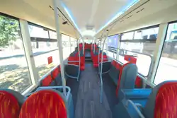 View down the saloon of Lynx's T29 KLN, refurbed R17 TYB, showing an ashy woodgrain flooring under seats upholstered in fiery moquette suspended from gleaming white saloon walls behind sweeping partitions with bright white LED uplighting above