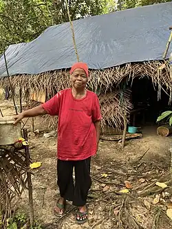 A Temuan woman stands in front of her traditional building