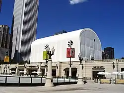A large white tent sits on the roof of a cafe building set in front of a skyscraper and blue sky.