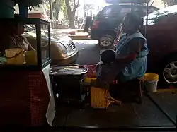 Woman preparing tlacoyos over the sidewalk in Colonia Condesa in Mexico City. The tlacoyo is cooked over a comal which is over an anafre, a kind of coal stove used in Mexican households without any heating energy