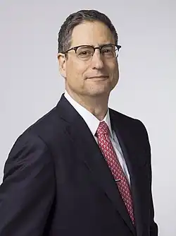 Tom Rothman wearing a suit and red tie, posing for a professional photo.