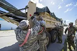 Daytime photograph of guardsmen securing a tarp on a dump truck filled with debris