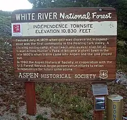 A brown wooden plaque with "White River National Forest" inscribed across the top and explanatory text about the Independence Townsite below
