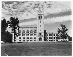 Black and white photo of a three-storey chateauesque-style building, with a belltower in the middle, a church in the left wing, and classrooms on the right wing