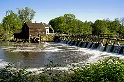 A large river flowing from a spillway; a mill in the background