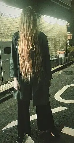 Wilson is standing in a dimly lit street in Tokyo, wearing dark clothing and with her hair down covering her face and torso. The photo overall has an omninous feeling.