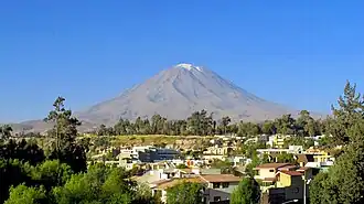 A brown conical mountain with a white summit rises above houses and parks