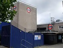 A grey building with a sign on it depicting a blue rectangle superimposed on a white circle superimposed on a red circle
