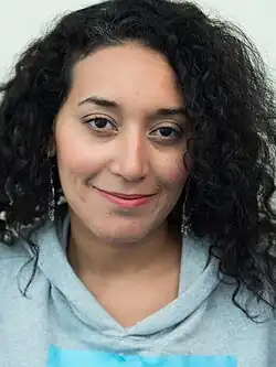 Portrait of Emna Mizouni at the Wikimedia Summit 2019. She is a dark-skinned woman with curly hair wearing a hoodie.
