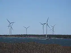 Seven three-blade wind turbines on the shore. A fishing boat is passing by.