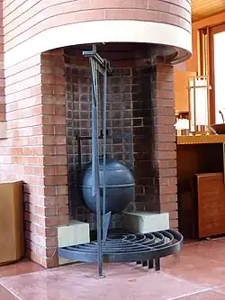 A hanging kettle under the rounded corner of the fireplace. The kettle is made of metal, while the fireplace is made of brick.